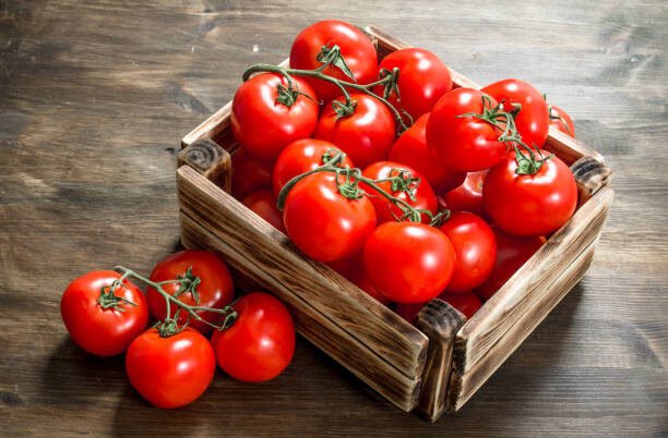 Fresh tomatoes in a box. On a wooden table.